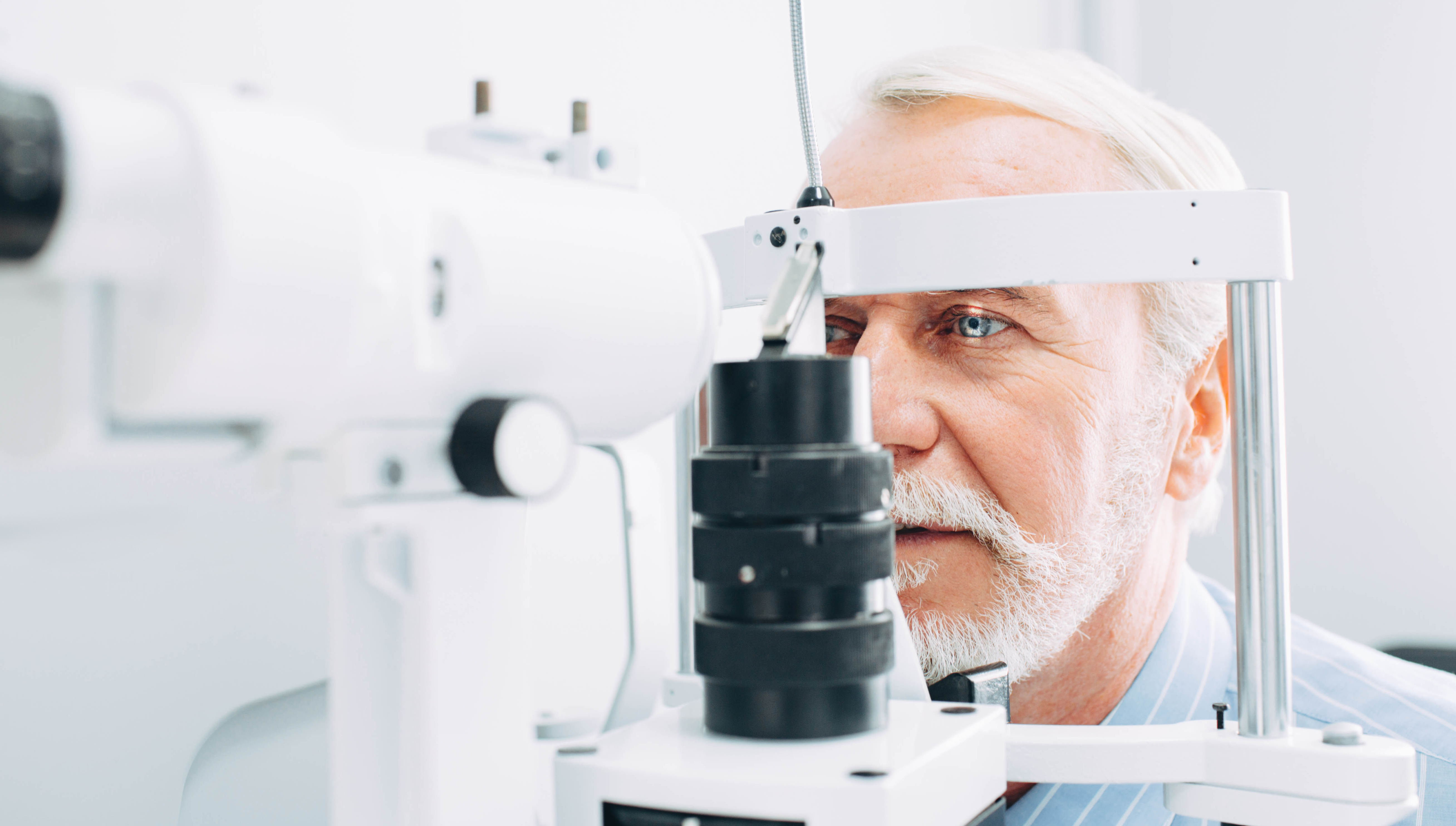 A man with white hair and beard looks into a medical device that shines a light into his eyes